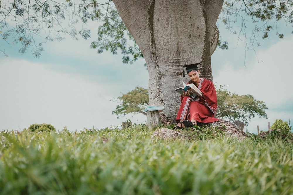 woman in red robe sitting under the tree and reading book