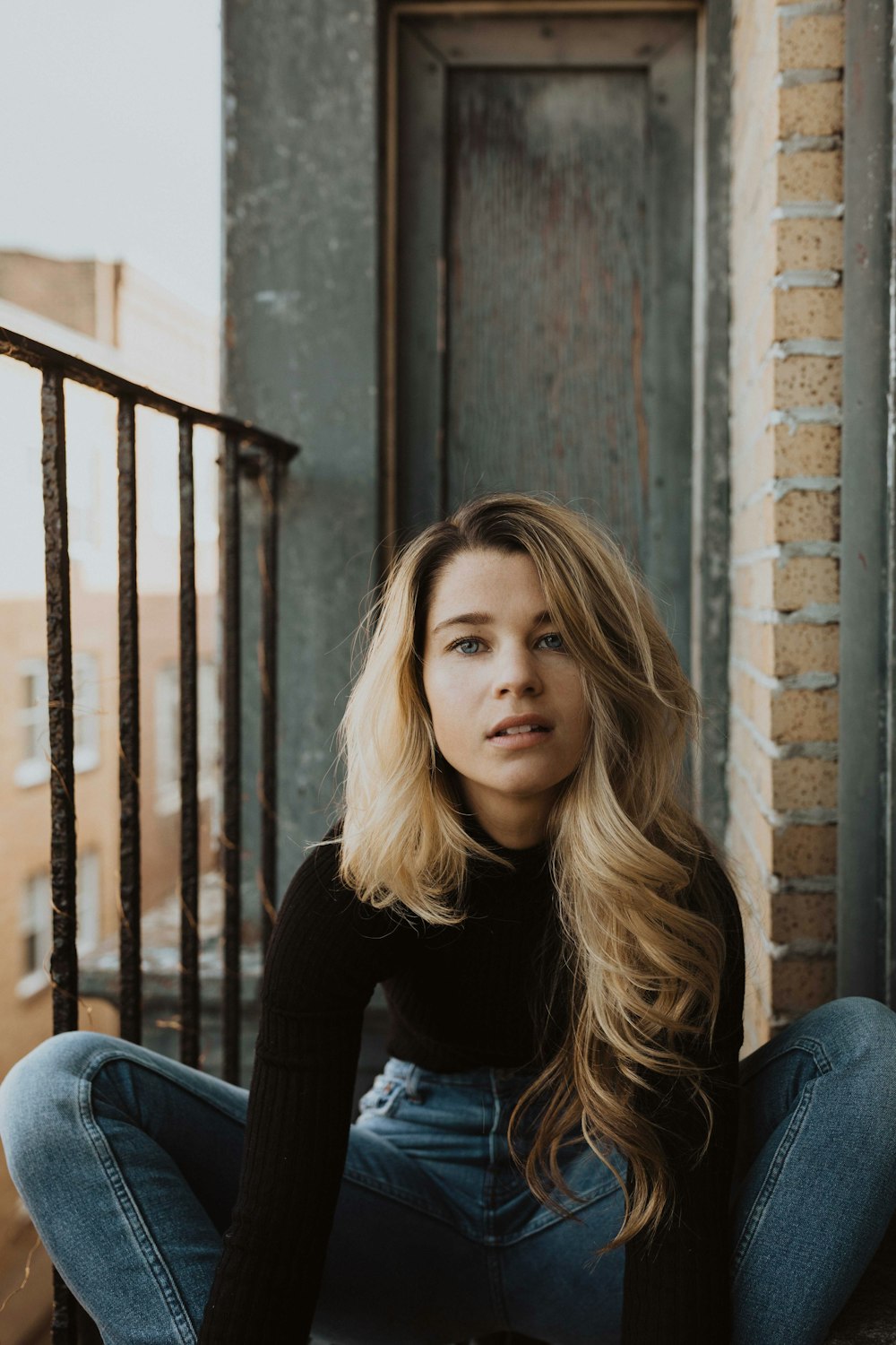 woman sitting beside rail near closed wooden door