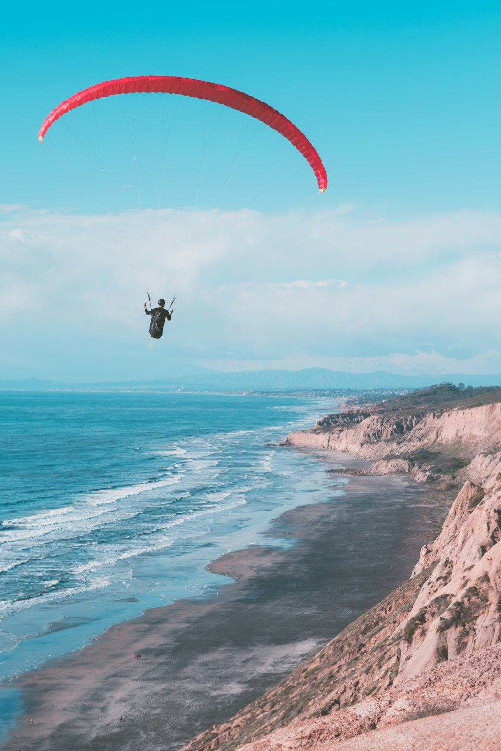 Une personne fait du parachute ascensionnel au-dessus de l’océan par une journée ensoleillée