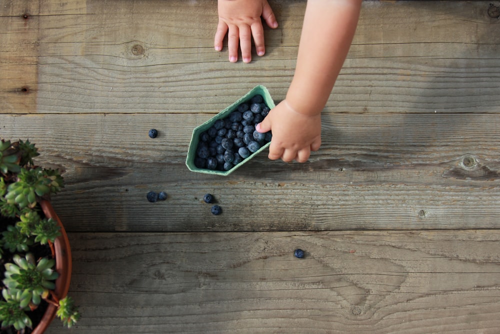 a child reaching into a bowl of blueberries