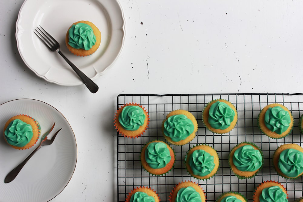 cupcakes with green toppings and two plate with one cupcake on top with fork on side