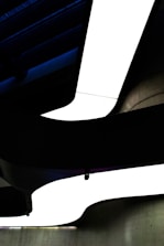 A modern architectural ceiling design featuring bold, curved lines with stark contrasts of light and shadow. The shapes create a dynamic sense of movement and depth.