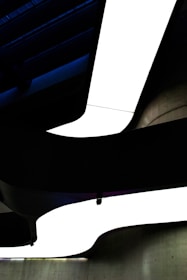 A modern architectural ceiling design featuring bold, curved lines with stark contrasts of light and shadow. The shapes create a dynamic sense of movement and depth.