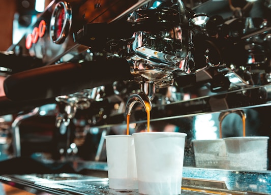 Instructor demonstrating espresso extraction with a group of engaged students around an espresso machine.
