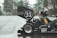 A driver wearing a helmet is seated in a small racing car with the number 31 marked on the rear wing. The car is parked on a wet pavement near a forested area, with trees visible in the background. The vehicle has logos from various sponsors including SKF, Lucas Oil, and Hoosier Tire.