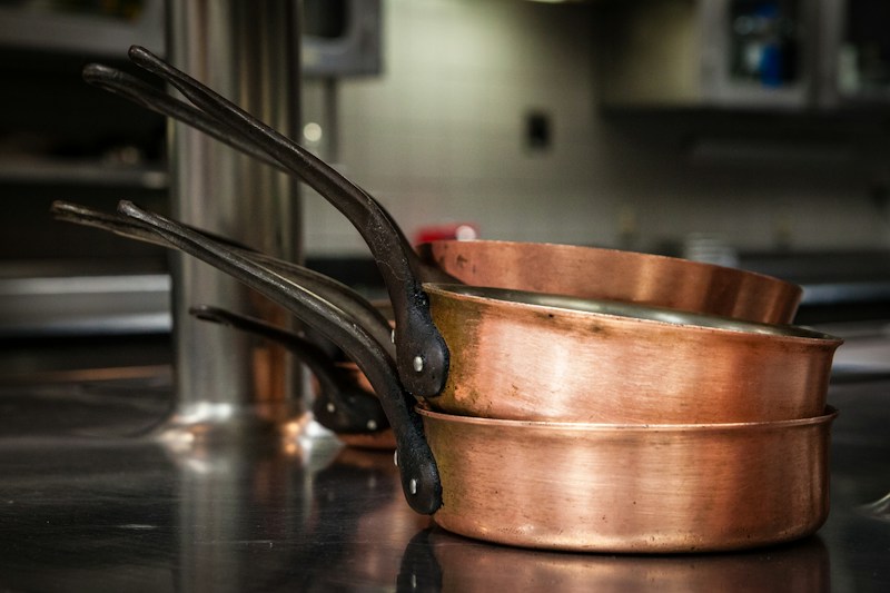 Three hammered copper pans stacked on a dark surface