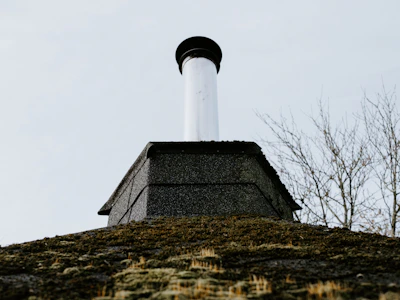 Technician inspecting flashing around a chimney on a cloudy day.