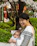 A smiling mother gently holding her baby wrapped in a soft, colorful baby wrap outdoors.