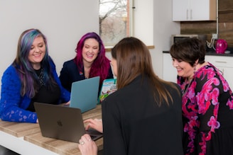 four woman on brown wooden table looking at laptops