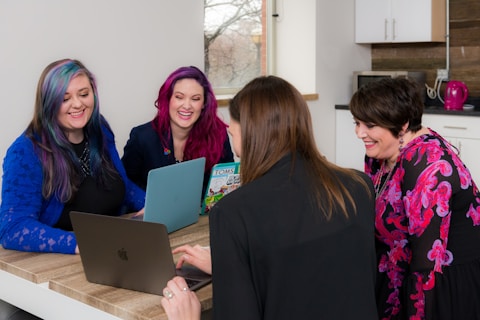 four woman on brown wooden table looking at laptops