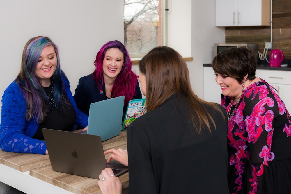 four woman on brown wooden table looking at laptops