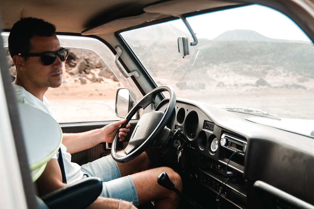 man wearing white crew-neck shirt holding steering wheel