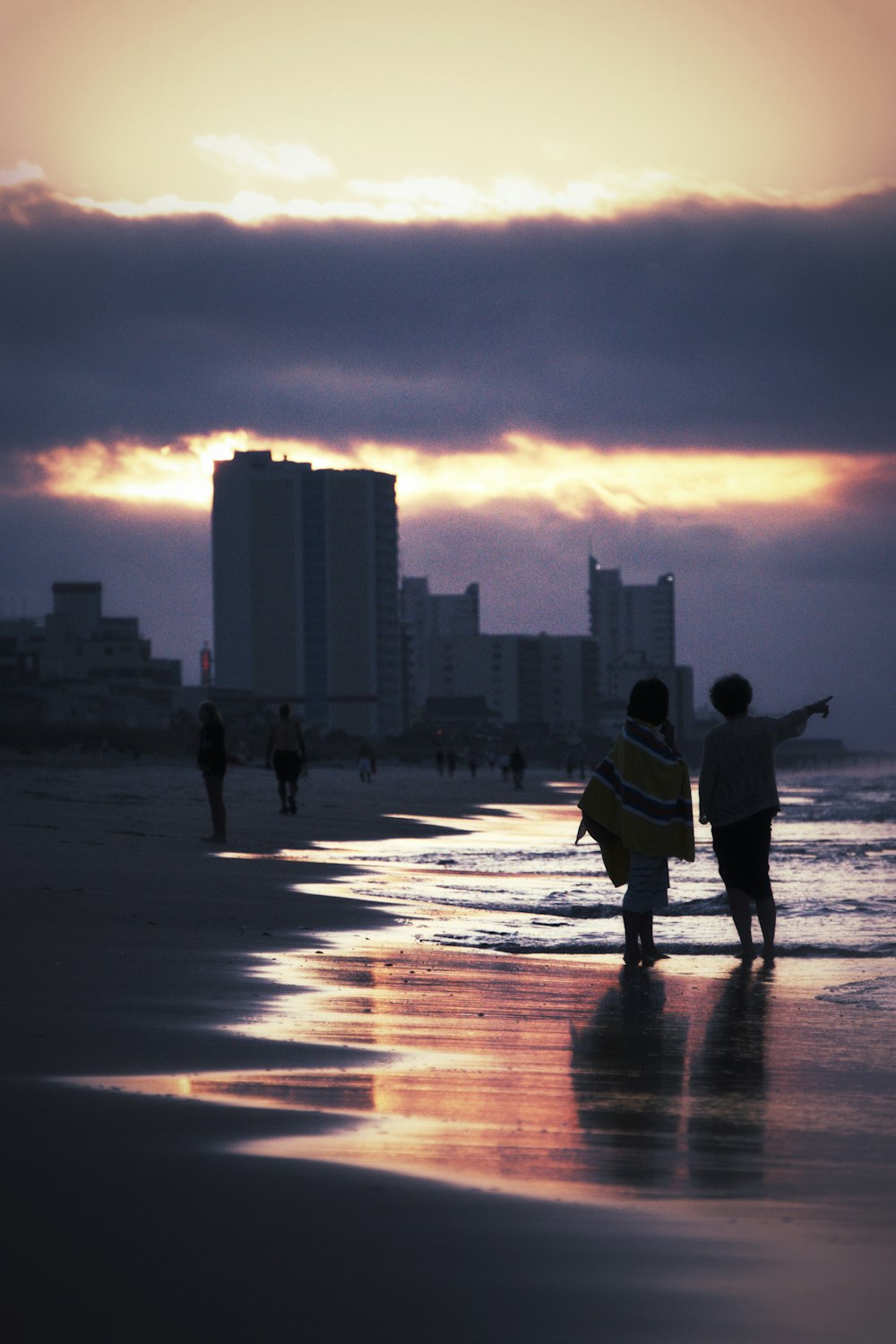two people walking on seashore near buildings during golden hour