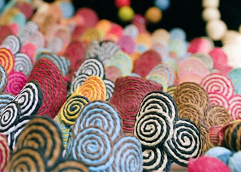 A vibrant, abstract composition featuring tightly coiled strings or fibers arranged in spirals. The spirals have a variety of colors including blue, red, yellow, black, and white, creating a dynamic and textured visual experience. The background appears blurred, enhancing the focus on the colorful spirals in the foreground.
