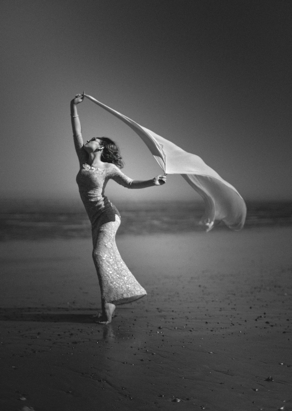 grayscale photography of woman standing on shore while holding scarf