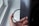 A hand is holding a circular camera filter near a window. The filter is labeled with markings that include 'B+W' and 'UV-Haze'. The background shows an out-of-focus window and wall, creating a soft lighting effect.