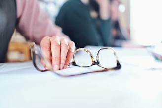 Close-up of hands holding a foam roller and blue light blocking glasses on a bedside table.