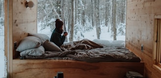 woman sitting on bed watching by the window during winter