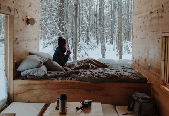 woman sitting on bed watching by the window during winter