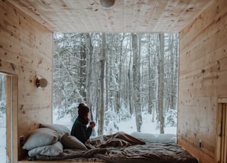 woman sitting on bed watching by the window during winter