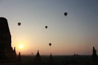 Silhouetted hot air balloons floating against a warm sunrise beige sky, with the silhouette of ancient ruins below.