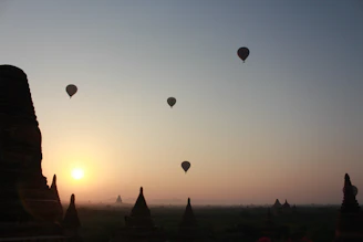 Silhouetted hot air balloons floating against a warm sunrise beige sky, with the silhouette of ancient ruins below.