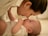A tender moment between an adult and a baby, where they are facing each other with noses almost touching, suggesting a close bond. The adult has a gentle expression, and the baby is lying on a soft surface, looking up with curiosity.