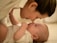 A tender moment between an adult and a baby, where they are facing each other with noses almost touching, suggesting a close bond. The adult has a gentle expression, and the baby is lying on a soft surface, looking up with curiosity.