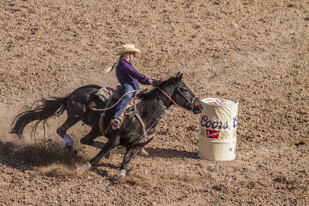 woman riding on black horse on brown field