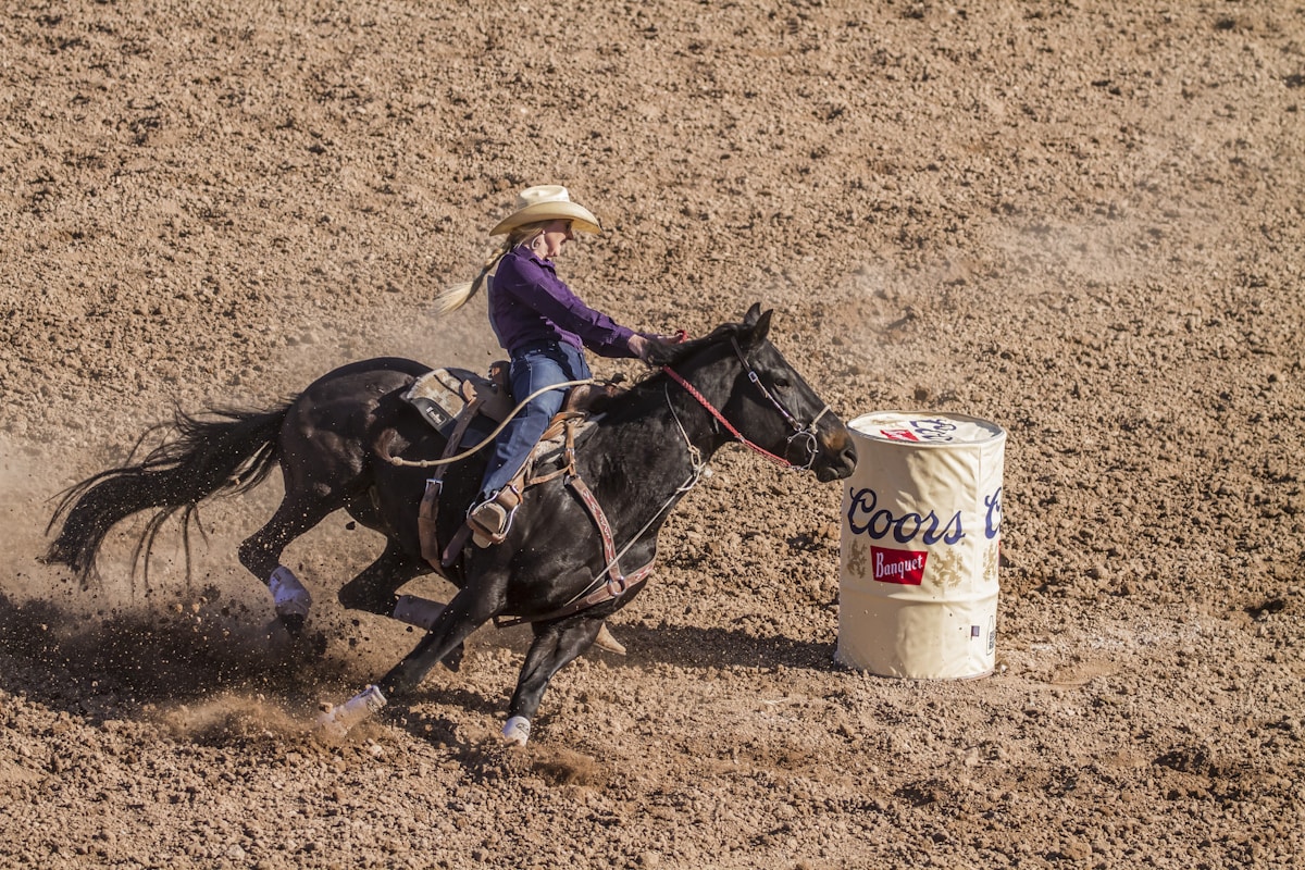 Cowgirl barrel racing on horseback in a rodeo arena