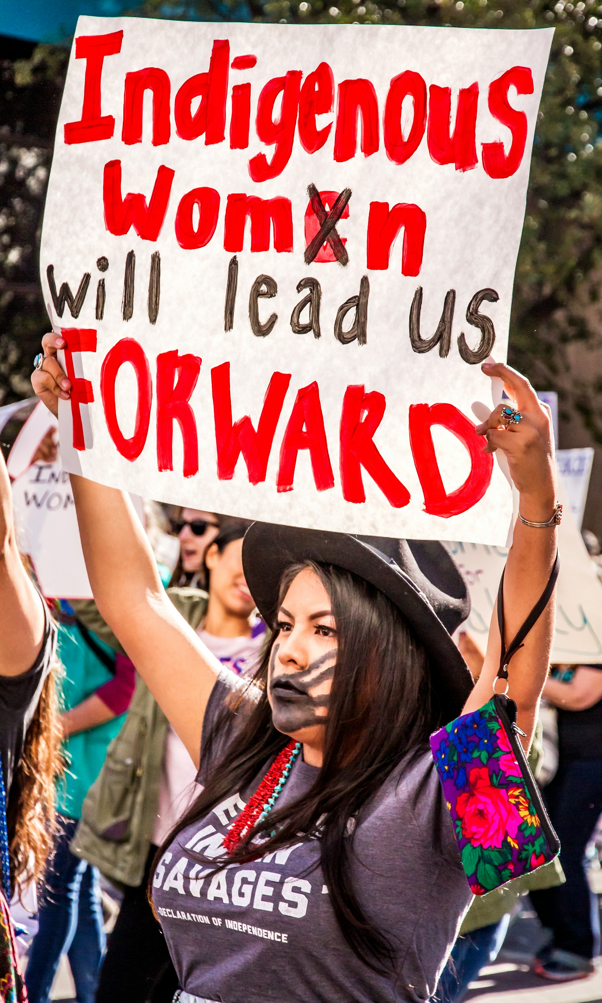 woman raising white and red sign with indigenous women will lead us forward text