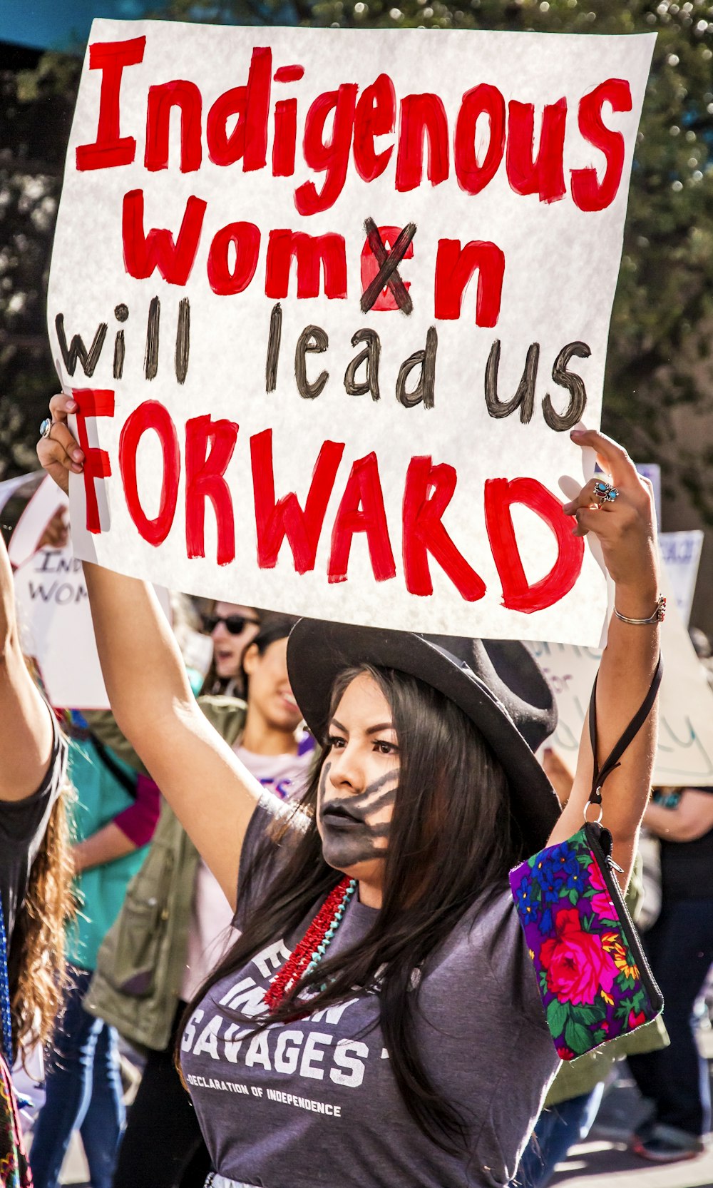 woman raising white and red sign with indigenous women will lead us forward text