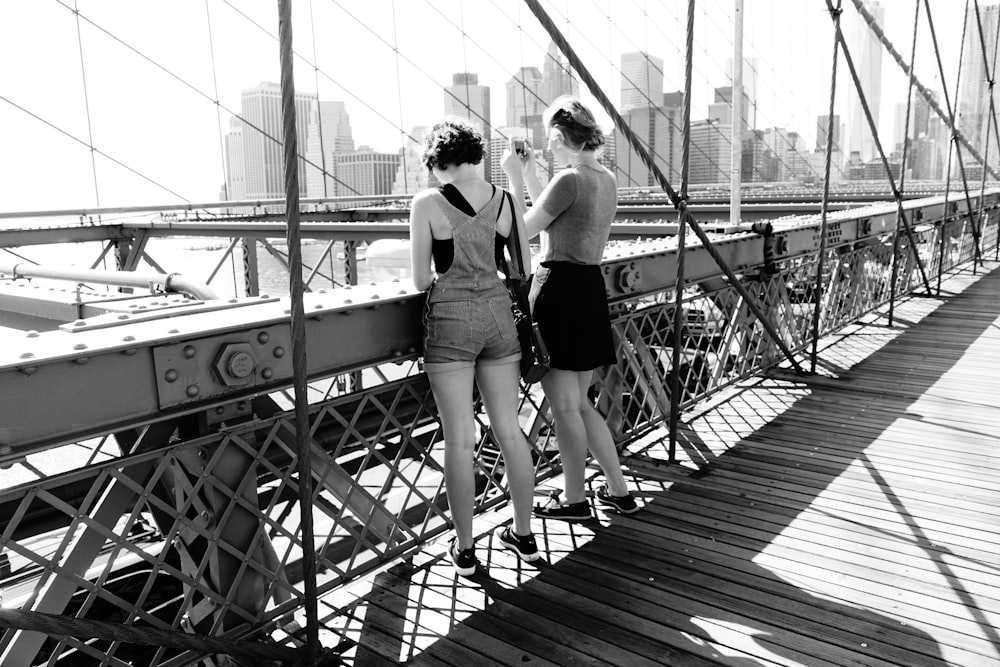 two roommates standing on the brooklyn bridge in nyc, looking over the river