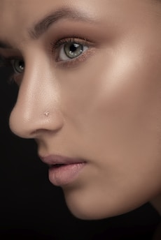 A close-up profile of a person's face, highlighting their eye, nose, and lips. The image captures the texture of the skin and the detail of the eyelashes. The background is a dark color, which brings the focus on the facial features.