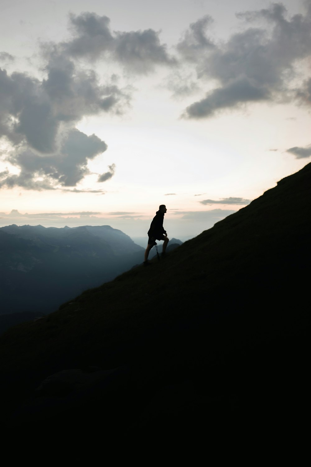 man climbing up the peak under grey cloudy sunset sky