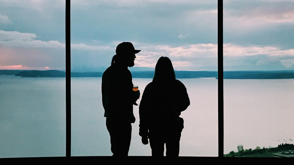 silhouette of two person standing near body of water