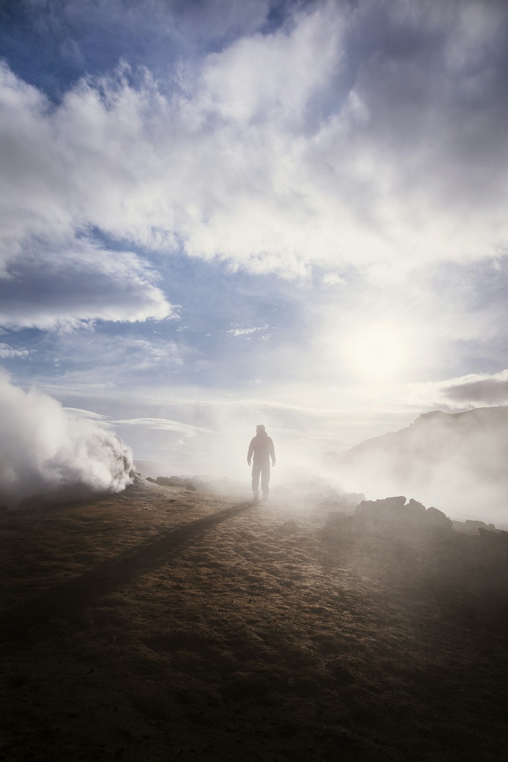 pessoa em pé perto da borda de uma montanha perto de nuvens durante o dia