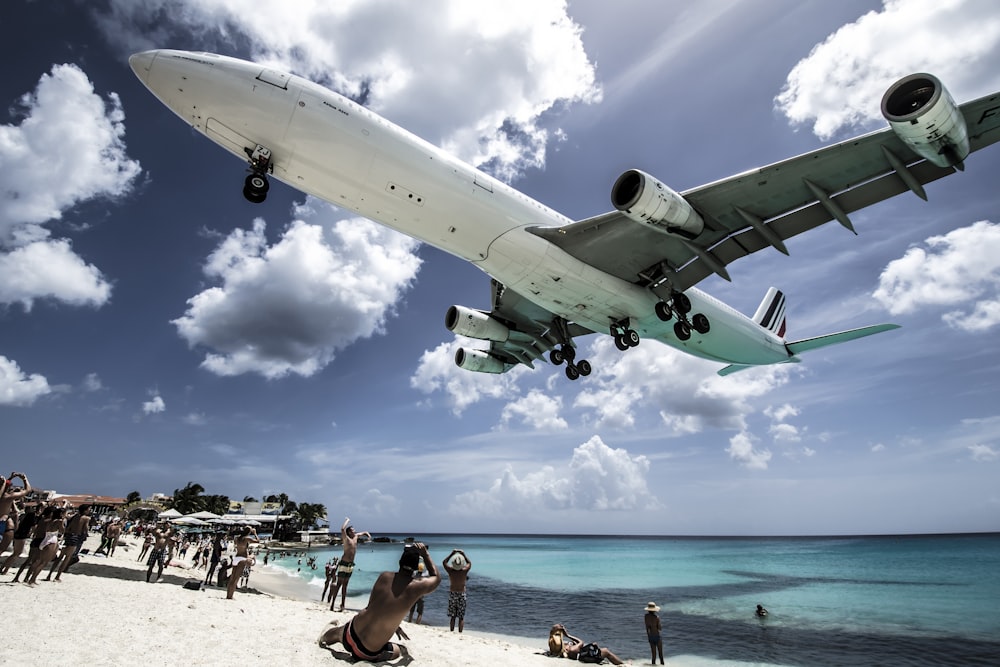 white airplane passing the people at the beach during daytime