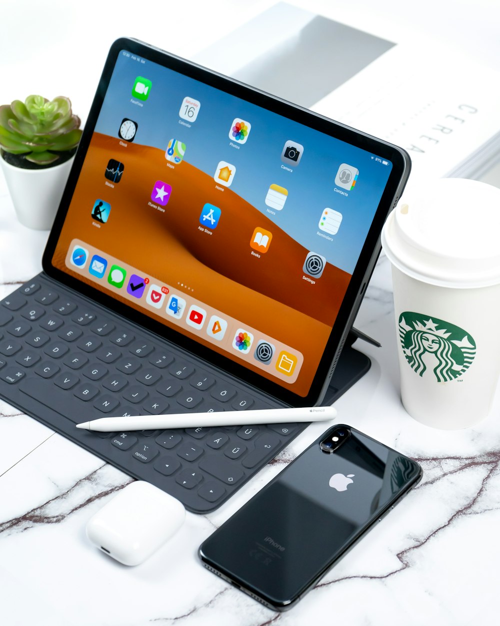 acceso iPad accanto a iPhone X grigio siderale e tazza di caffè Starbucks