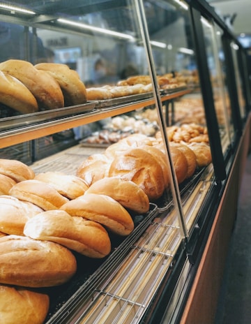 A bakery display case filled with various types of bread, including rolls and loaves, arranged neatly on metal racks within a glass enclosure.
