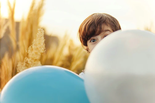 A close-up of a child’s curious eyes peeking through colorful balloons.