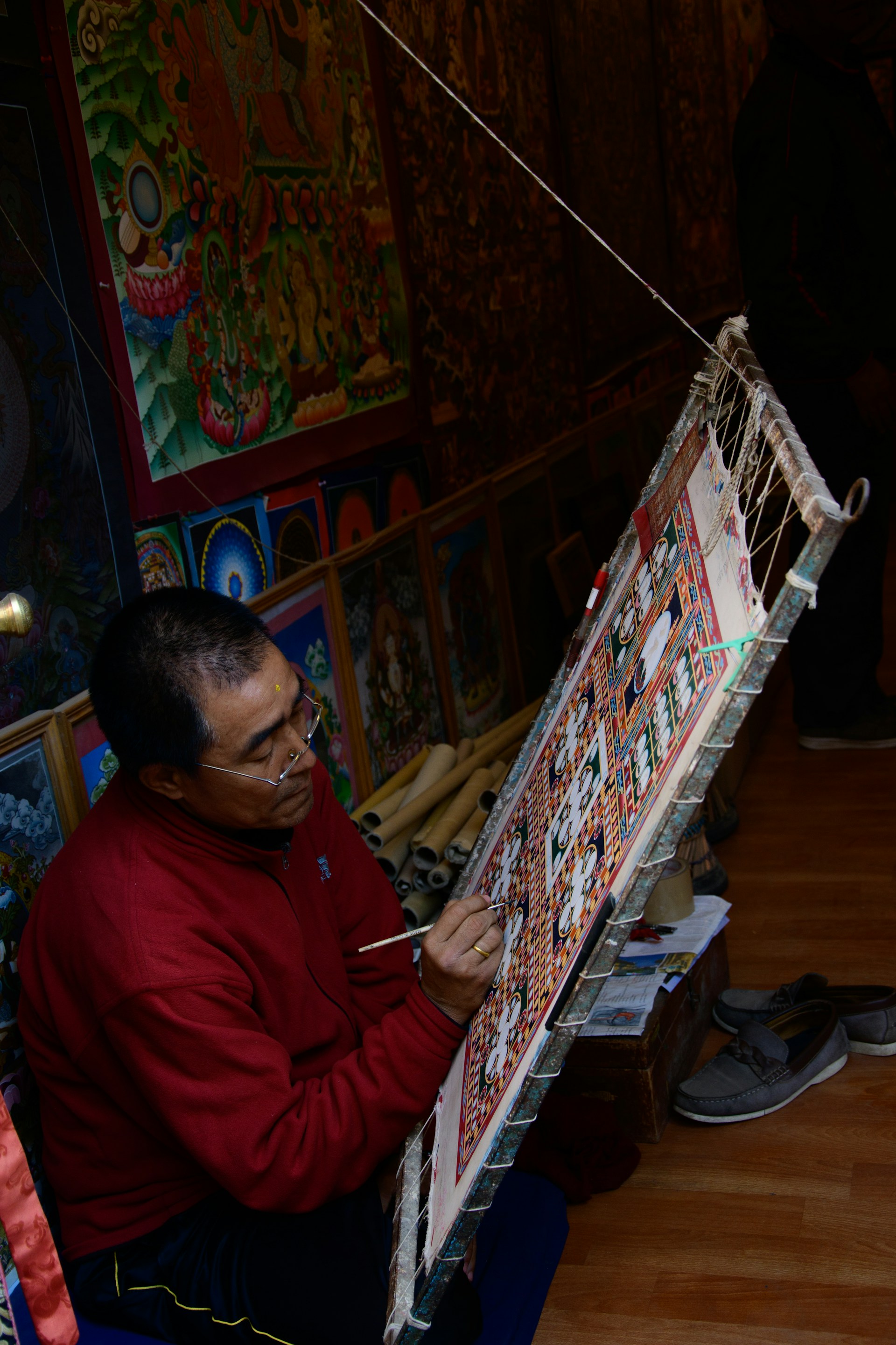 An atmospheric photograph of a Mithila artist at work, surrounded by traditional tools and natural dyes, immersed in the creation of a vibrant mural.