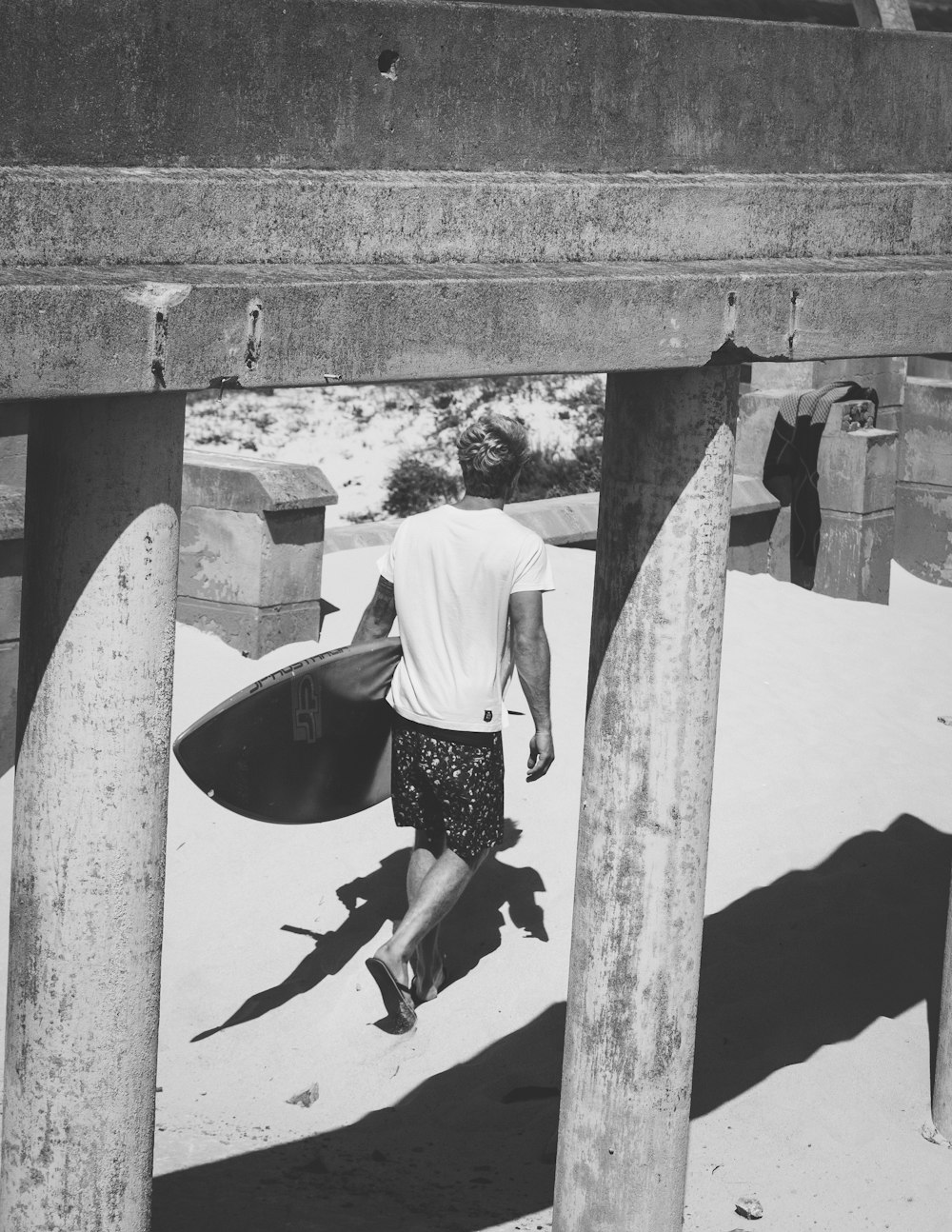 Photographie en niveaux de gris d’un homme tenant une planche de surf