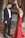 A couple engaged in a dance, with the man wearing a formal black suit and bow tie and the woman in a long red dress. They are standing on a tiled floor with dry leaves scattered around, possibly in an outdoor or historical setting with stone walls.