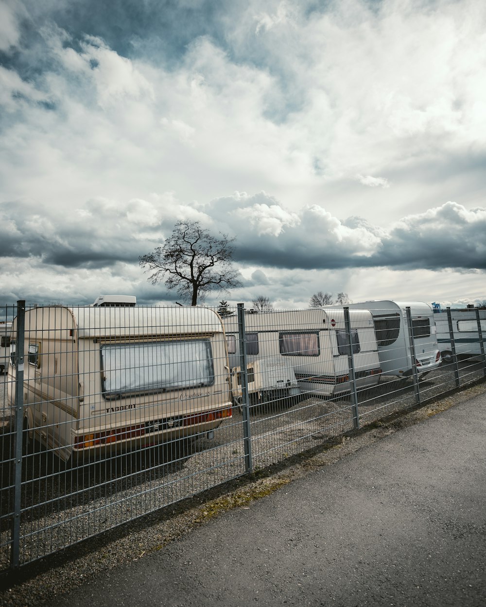 parked white camper trailers beside fence under cloudy sky during daytime