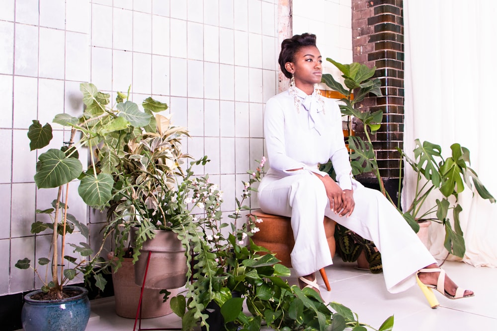 sitting woman wearing withe long-sleeved shirt and pants surrounded by plants