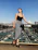 A smiling woman wearing a sleek, modern outfit from zarmtam prime, standing confidently in a sunlit urban setting.