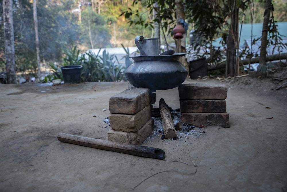 black clay pot on top of bricks with burning firewood on bottom