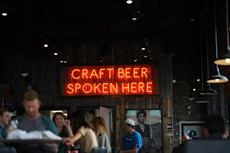 people beisde neon lighted Craft Beer spoken here signage