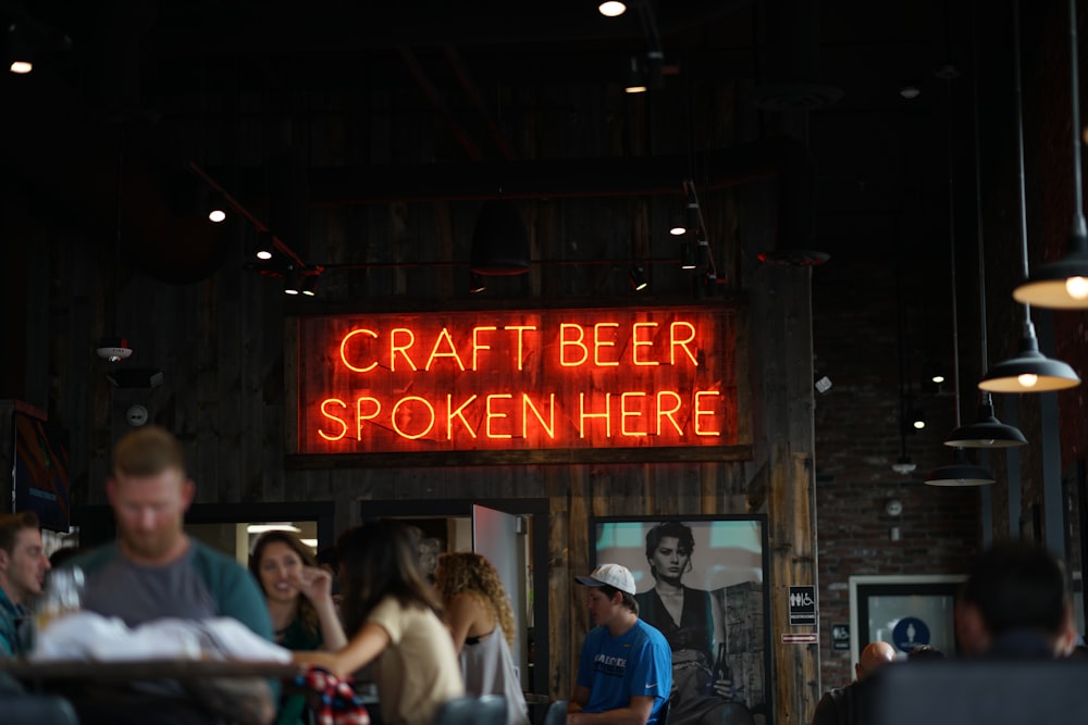 people beisde neon lighted Craft Beer spoken here signage